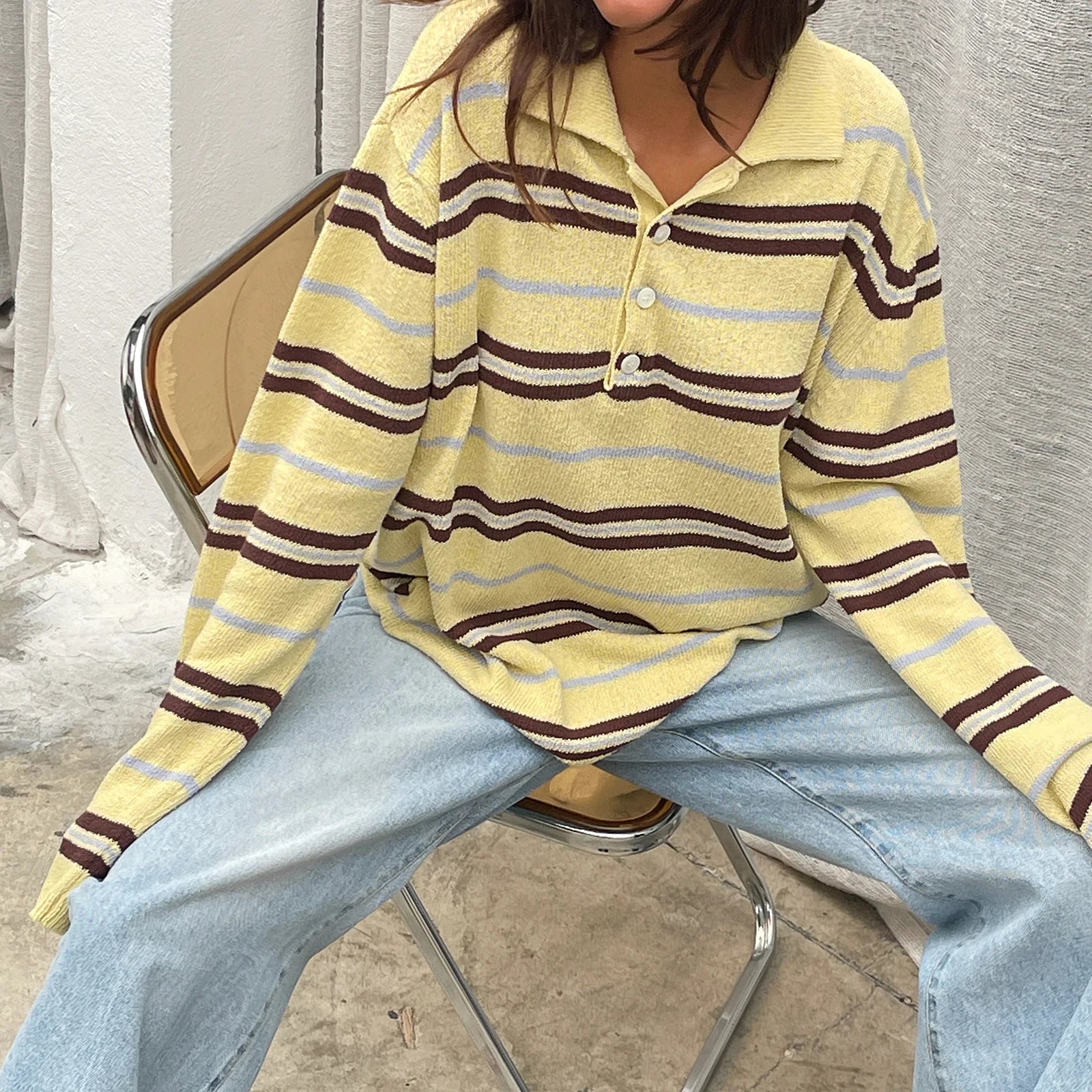 Person wearing a yellow striped sweater and light blue jeans sitting on a chair.