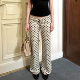 Person wearing polka dot pants holding a beige handbag indoors.