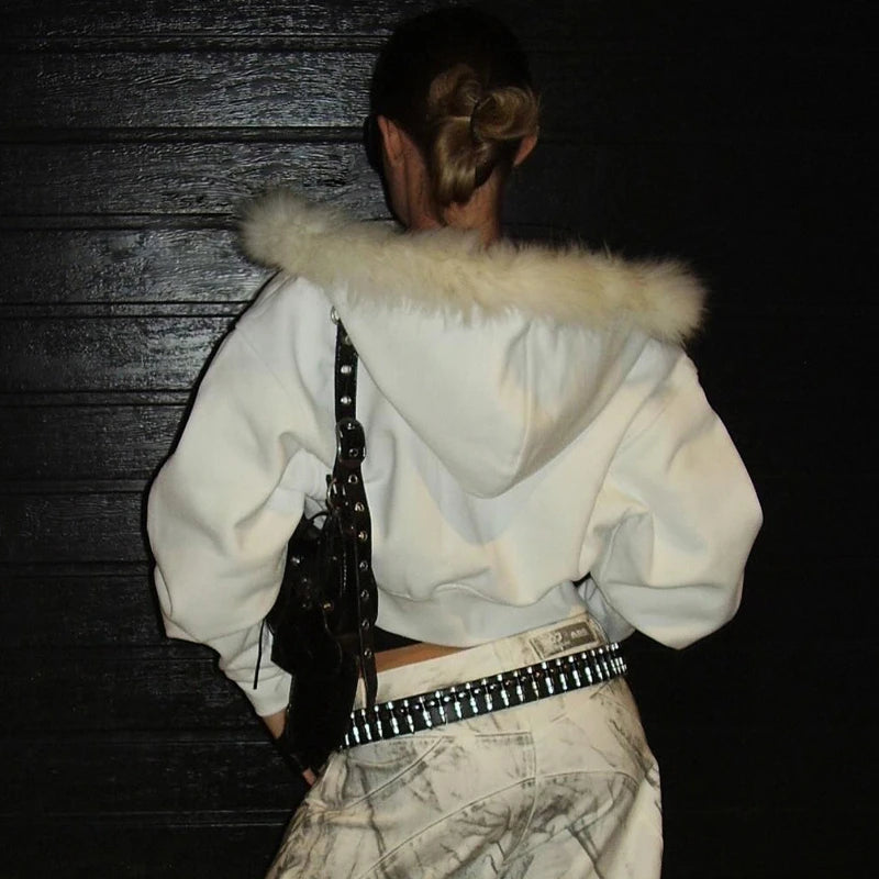 Person wearing a white hoodie with fur trim, holding a guitar, against a dark background.