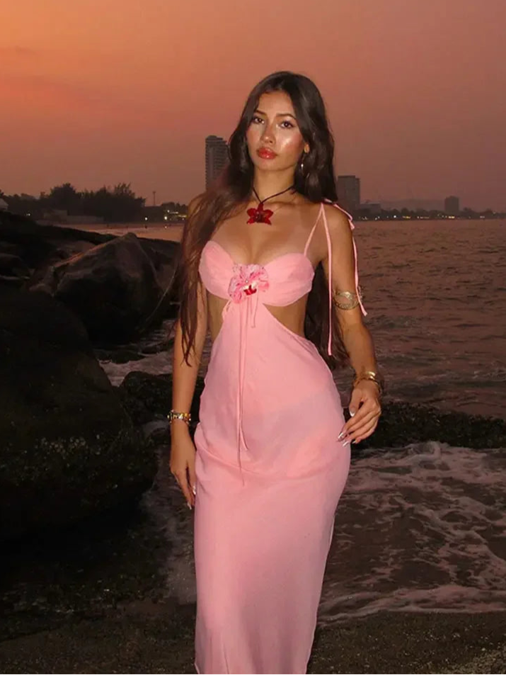 Woman in a pink dress standing by the water at sunset.