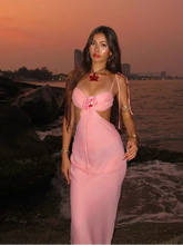 Woman in a pink dress standing by the water at sunset.