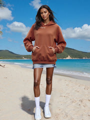 Woman wearing a brown hoodie on a beach with blue sky and ocean