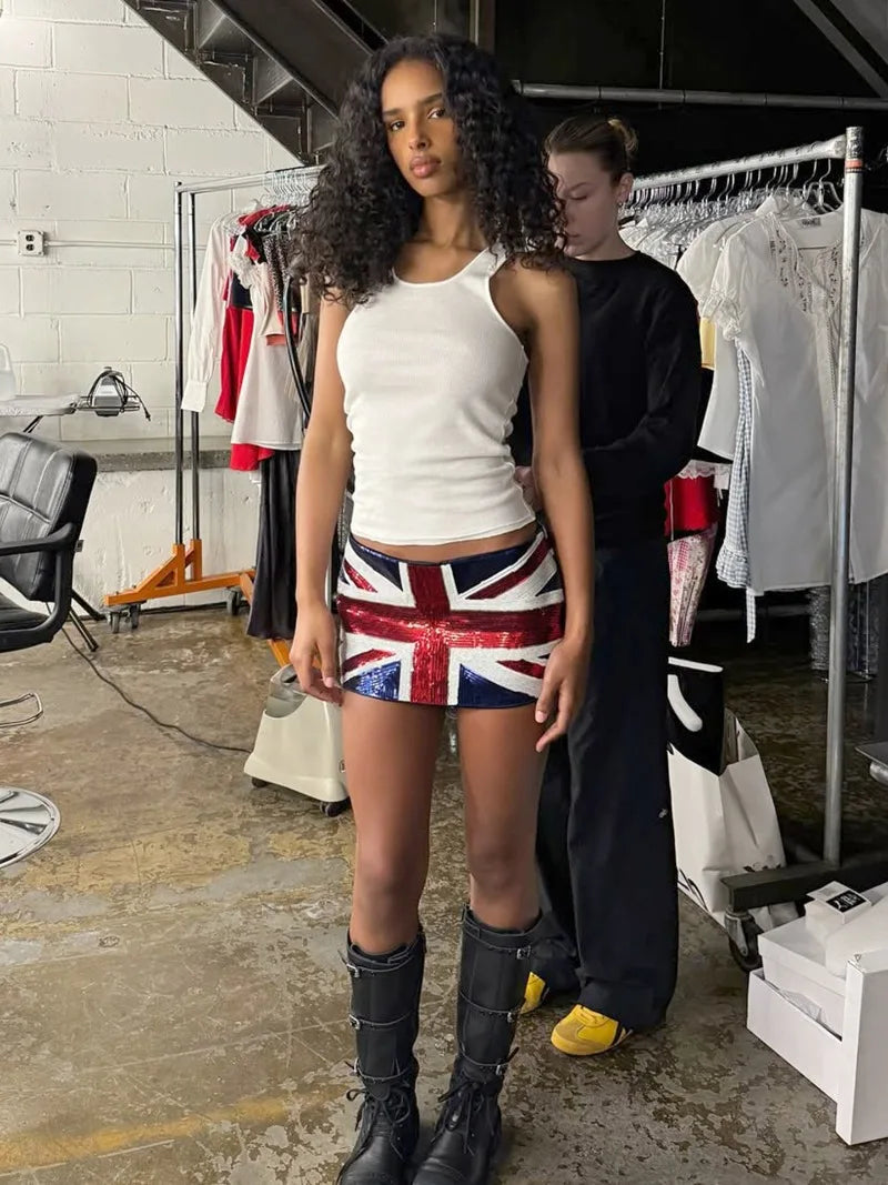 Woman wearing a Union Jack skirt in a backstage area with clothing racks and people.