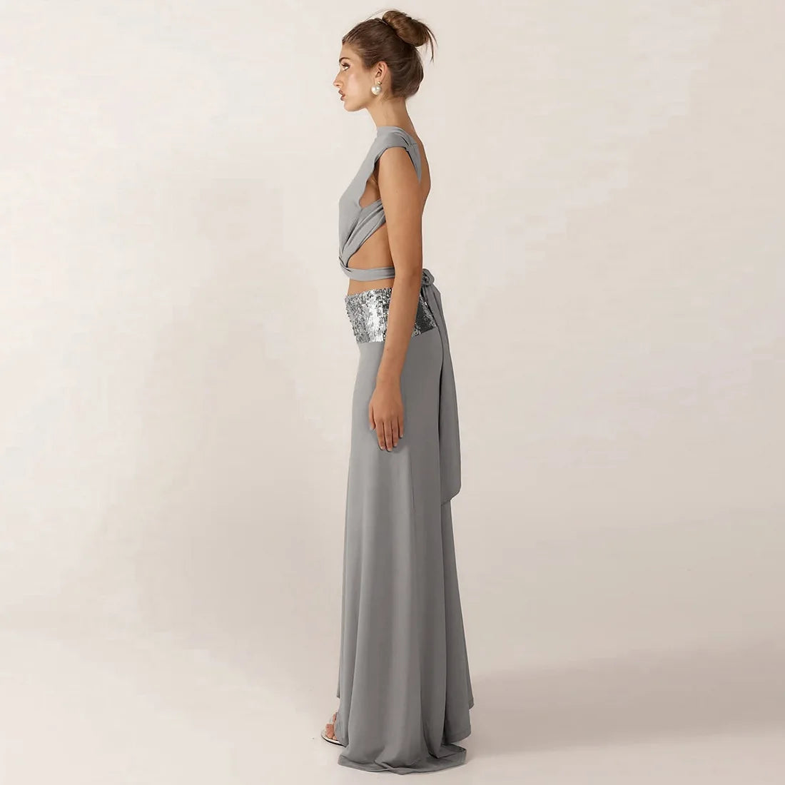 Woman wearing a gray evening gown with a sequined waistband on a plain background