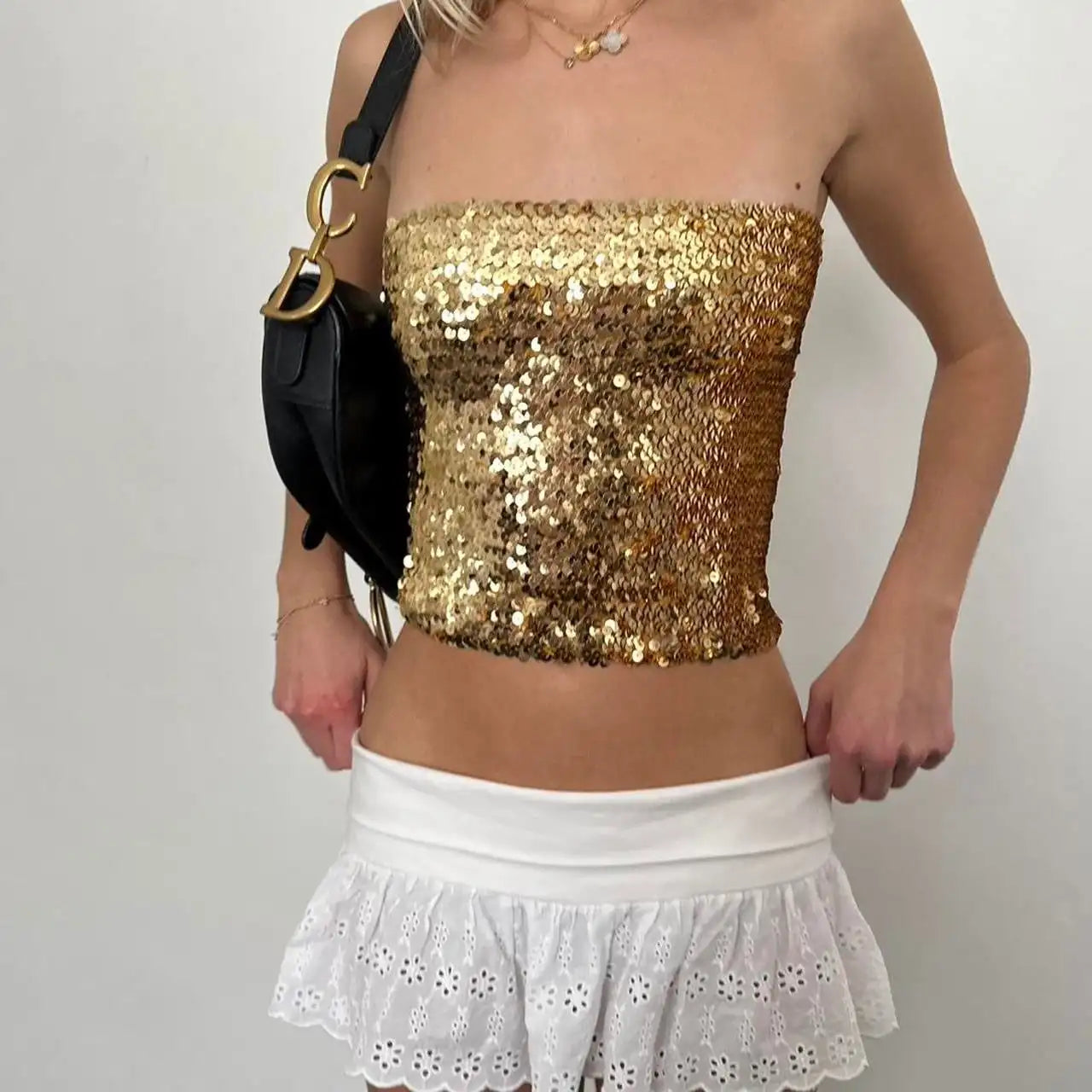 Person wearing a gold sequin top and white skirt with a black handbag - full view