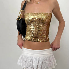 Person wearing a gold sequin top and white skirt with a black handbag - full view