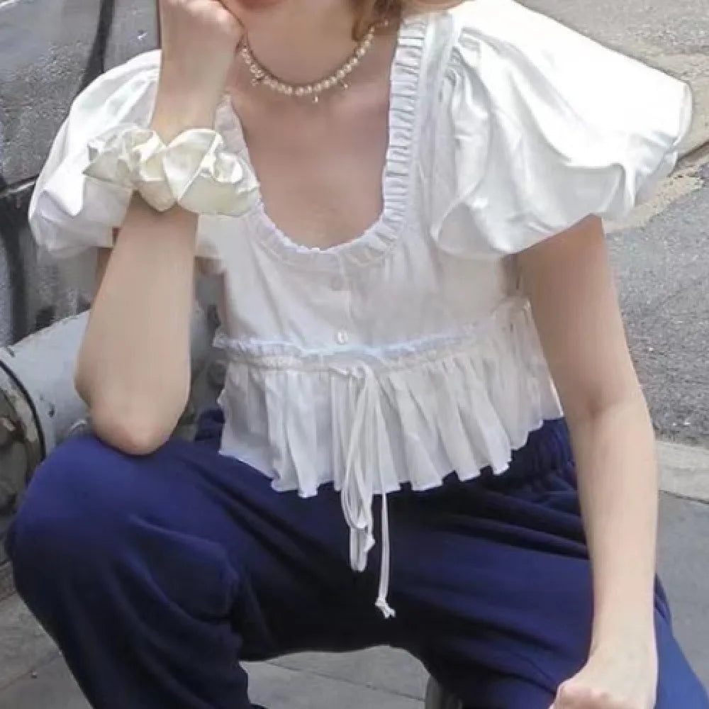 Person wearing a white blouse with ruffled details and blue pants sitting on a bench.