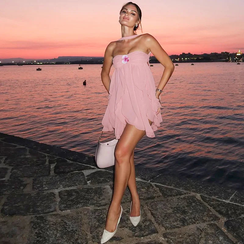 Woman in a pink dress standing by a waterfront at sunset