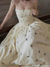 White strapless dress with black bow details on a wooden floor.