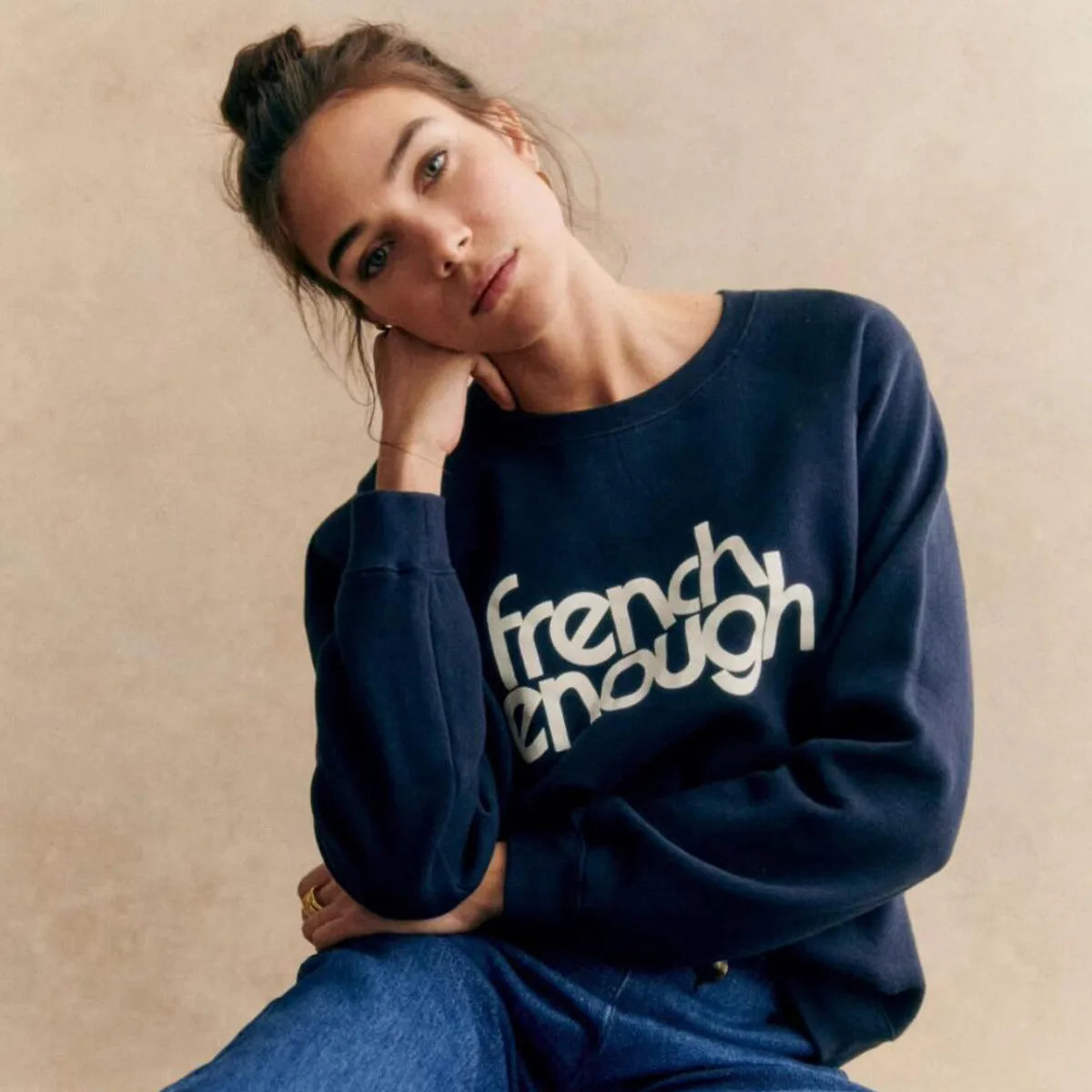 Woman wearing a navy blue sweatshirt with 'french enough' text on a beige background
