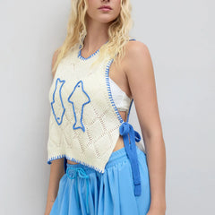 Woman wearing a white crochet top with blue accents and blue pants on a light gray background