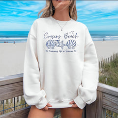 Person wearing a white sweatshirt with beach-themed design at a beach setting