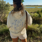 Person wearing a white hoodie with blue graphics in a natural setting