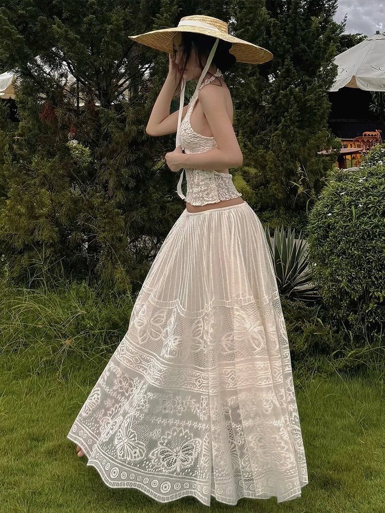 Woman in a white lace dress and sun hat standing in a garden.