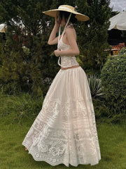 Woman in a white lace dress and sun hat standing in a garden.
