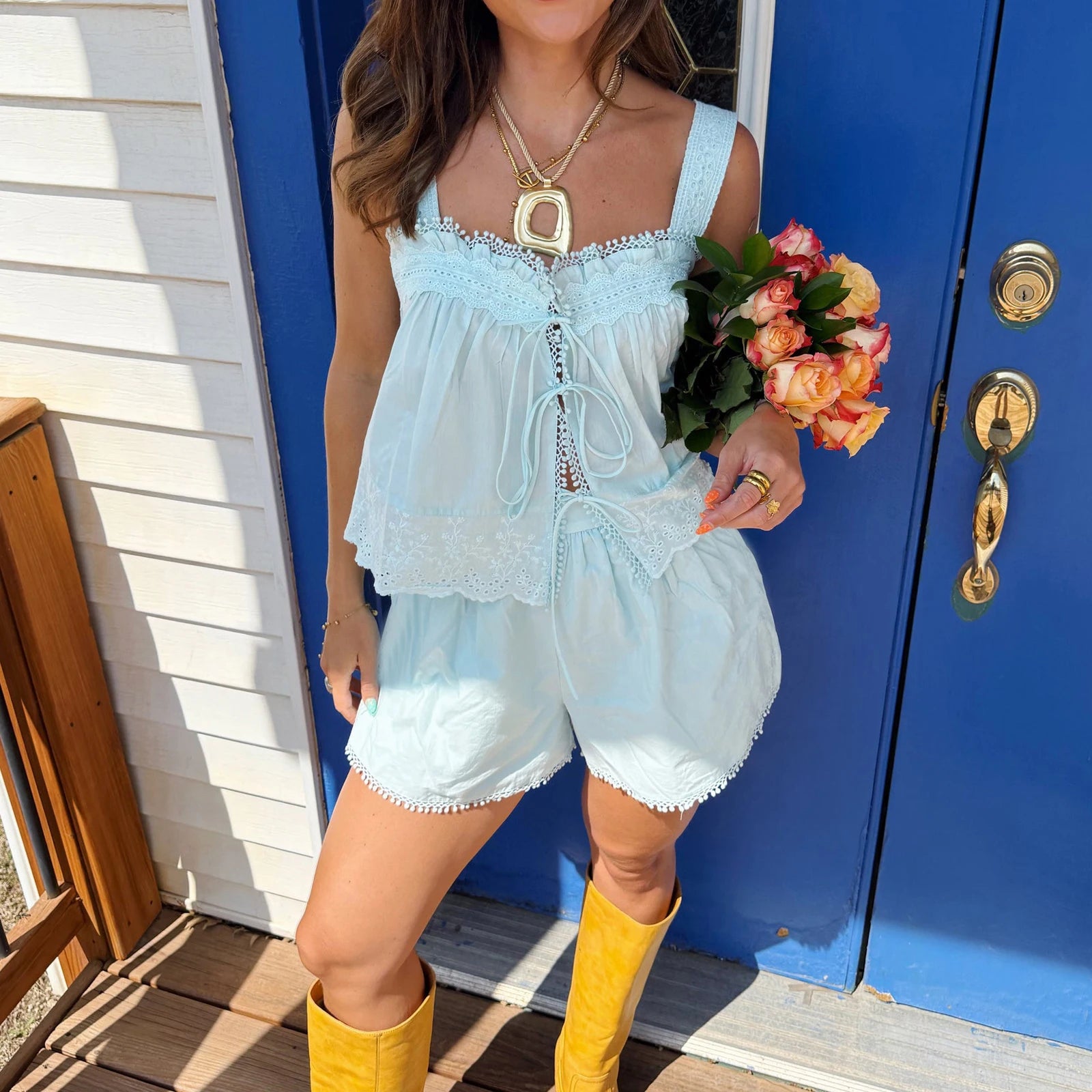 Woman in light blue dress and yellow boots holding flowers in front of a blue door.