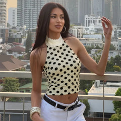 Woman in a polka dot top and white pants standing on a balcony with a cityscape background