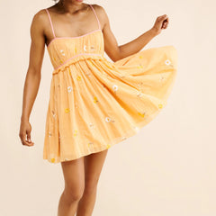 Woman wearing a yellow dress with floral embellishments on a beige background