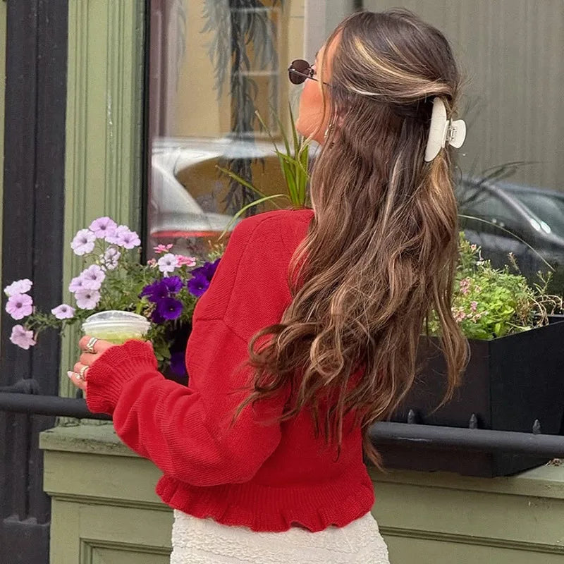 Woman in a red sweater holding a drink, standing next to a window with plants.