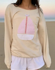 Beige sweatshirt with pink sailboat design on a beach background