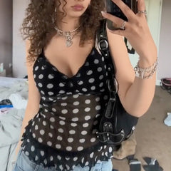 Person wearing a black polka dot top taking a mirror selfie.