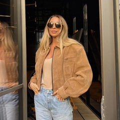 Woman wearing a tan jacket and sunglasses, standing in front of a glass door.
