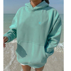 Person wearing a light blue hoodie with a star logo on a beach