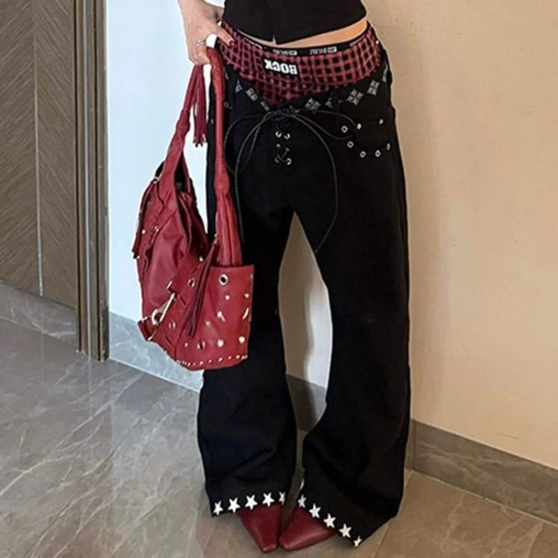 Person wearing black pants with star details and holding a red handbag indoors.