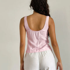 Person wearing a pink tank top with lace details on a plain background