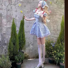 Person in a checkered dress standing outdoors with plants and a textured wall background