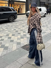 Person wearing a plaid shirt and Adidas tracksuit on a city street.