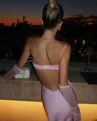 Woman in a pink dress with an open back standing on a rooftop at sunset.