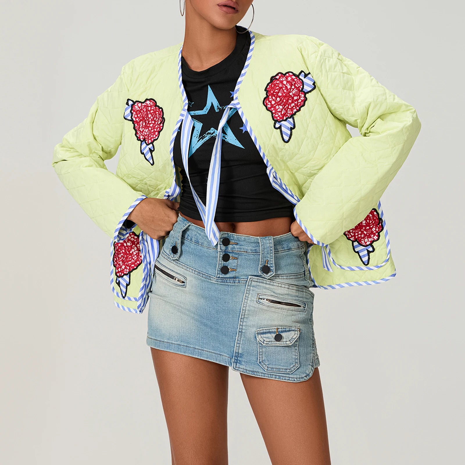 Person wearing a light green quilted jacket with ice cream cone designs, black crop top, and denim skirt on a plain background.