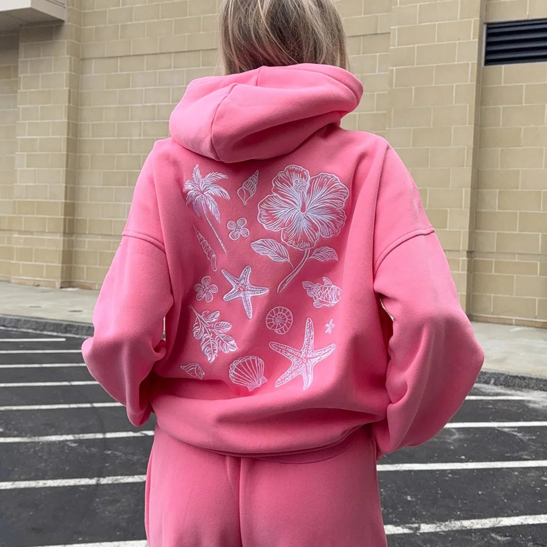 Person wearing a pink hoodie with floral and beach-themed designs outdoors.