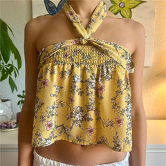 Yellow floral halter top worn by a person indoors with a plant and lamp in the background.