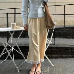 Person wearing a light blue cardigan and beige skirt with lace trim, standing outdoors.