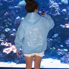 Person wearing a light blue hoodie with marine animal designs, taking a photo of an aquarium.
