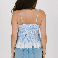Woman wearing a blue floral camisole with lace trim on a plain background