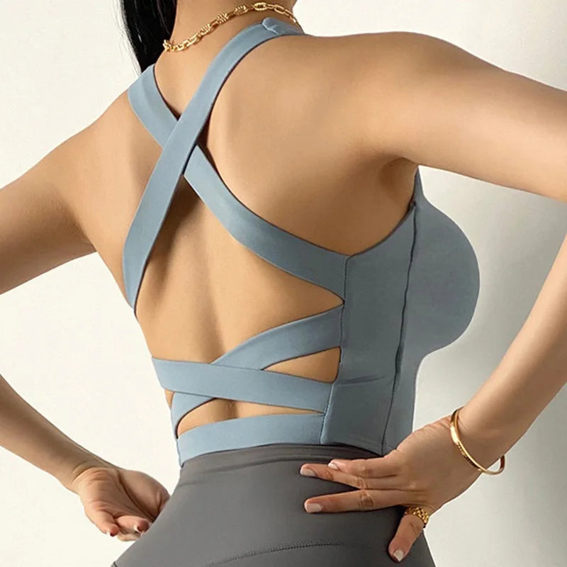 Woman wearing a gray sports bra and leggings with criss-cross straps on a light background