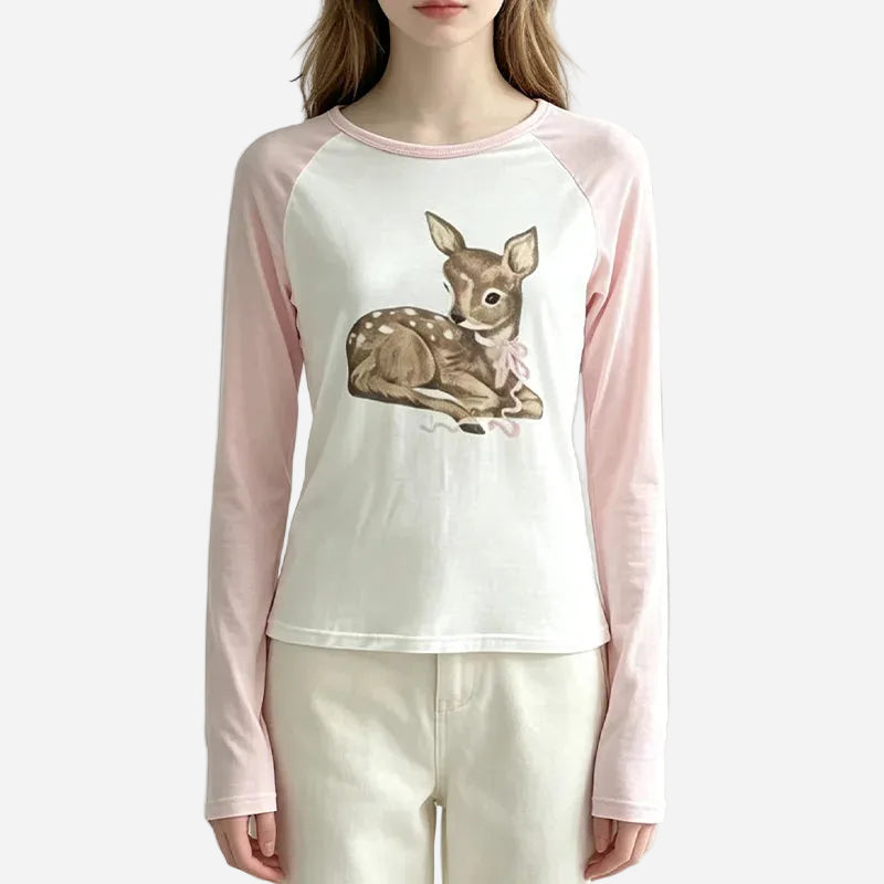 A woman wearing a long-sleeve raglan top with a white body, light pink sleeves, and a central graphic of a brown deer with a pink bow. The Anivia brand logo is visible in the top left corner.