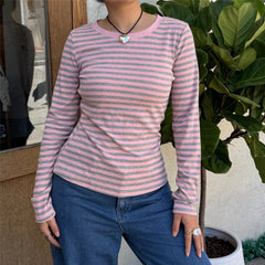 Person wearing a pink and gray striped long-sleeve shirt and blue jeans standing outdoors.