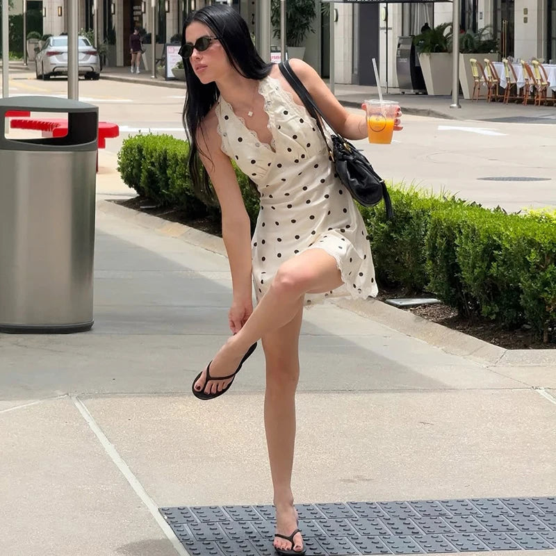 Woman in a white polka dot dress posing on a city sidewalk.