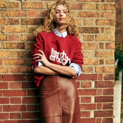 Woman wearing a red sweater with text standing against a brick wall