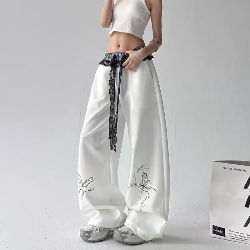White wide-leg pants with butterfly embroidery and lace details worn by a person on a gray background.