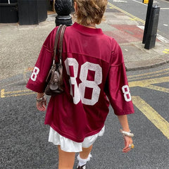 Person wearing a maroon sports jacket with large white numbers on a street.