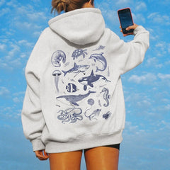 Person wearing a hoodie with marine animal illustrations against a blue sky.