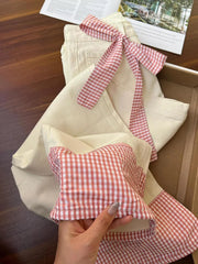 Beige jeans with red and white checkered accents held by a hand on a wooden surface.