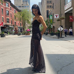 Woman in a black polka dot dress standing on a city street.