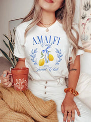 A woman wearing a comfortable graphic t-shirt featuring an Amalfi Coast design, paired with white trousers for a casual look.