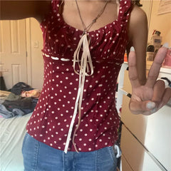 Person wearing a red polka dot top with a bow, standing in a room.